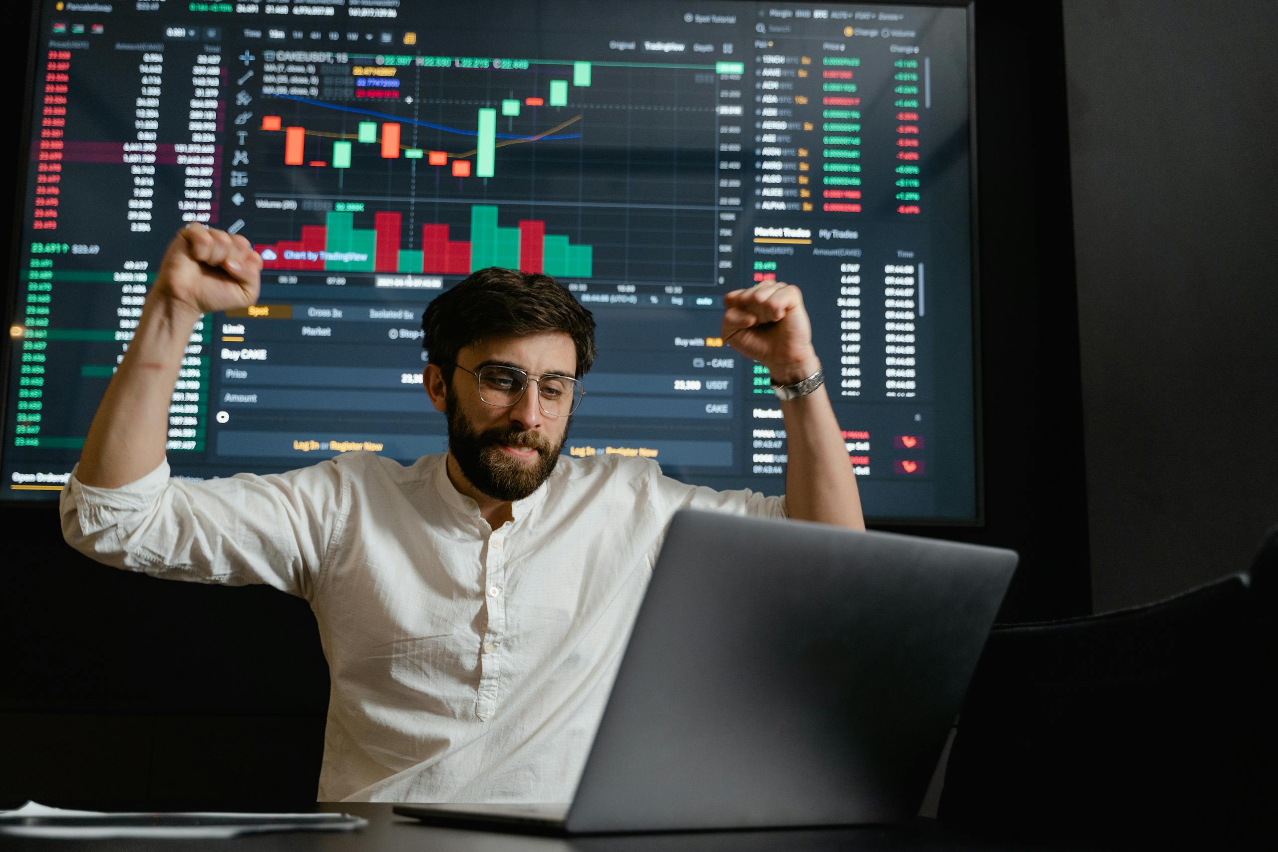 Successful businessman exults in front of a stock market display.